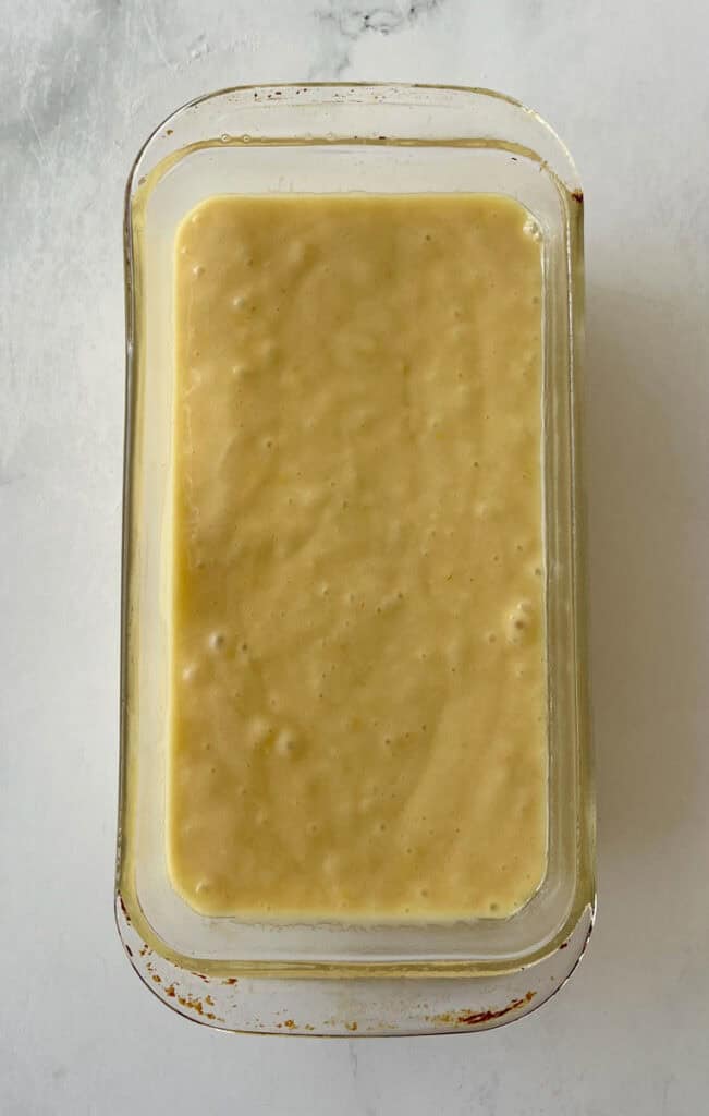 Lemon loaf batter in a rectangular baking glass dish on a marbled surface.