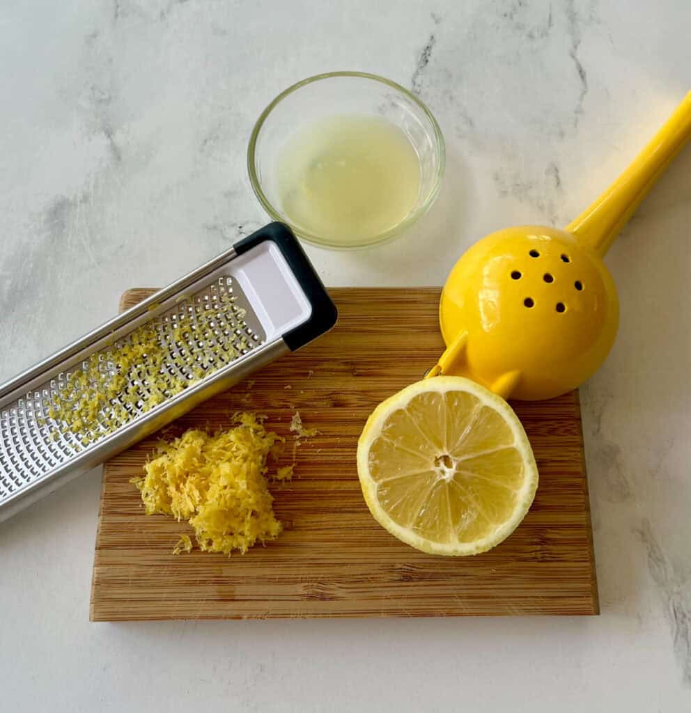 Fresh lemon and zest being grated with a yellow citrus zester.