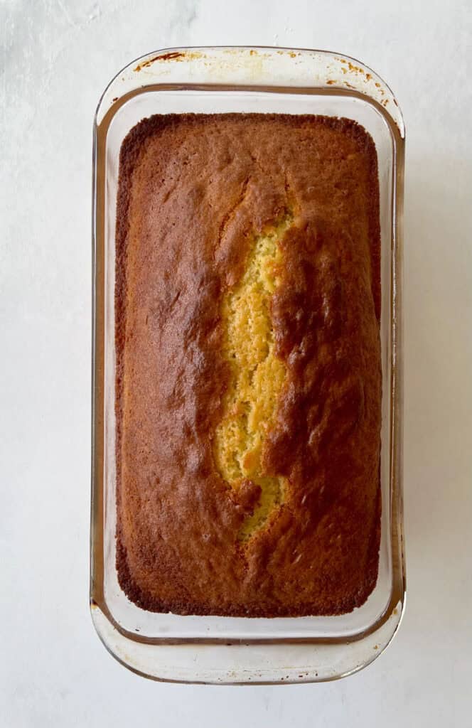 Freshly baked lemon loaf in a rectangular glass baking dish on a marbled surface.