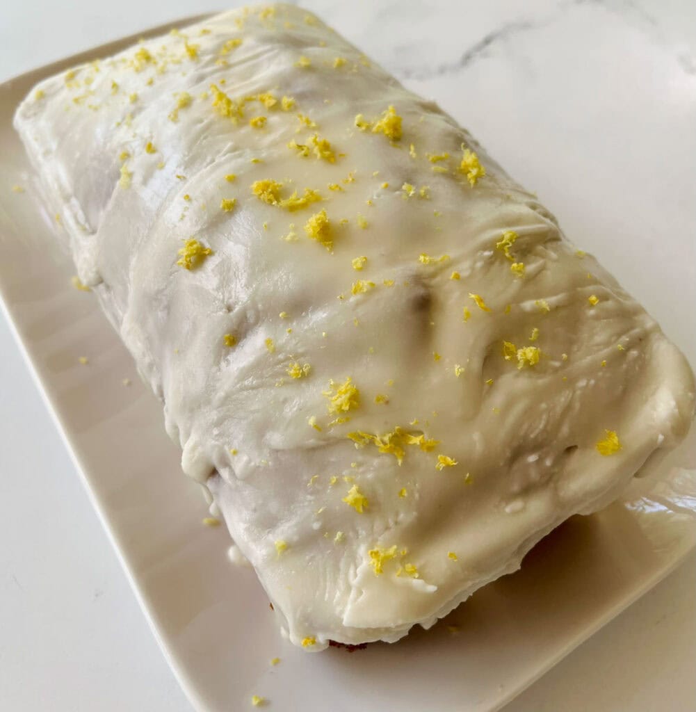 A rectangular lemon loaf covered with white icing and sprinkled with lemon zest.