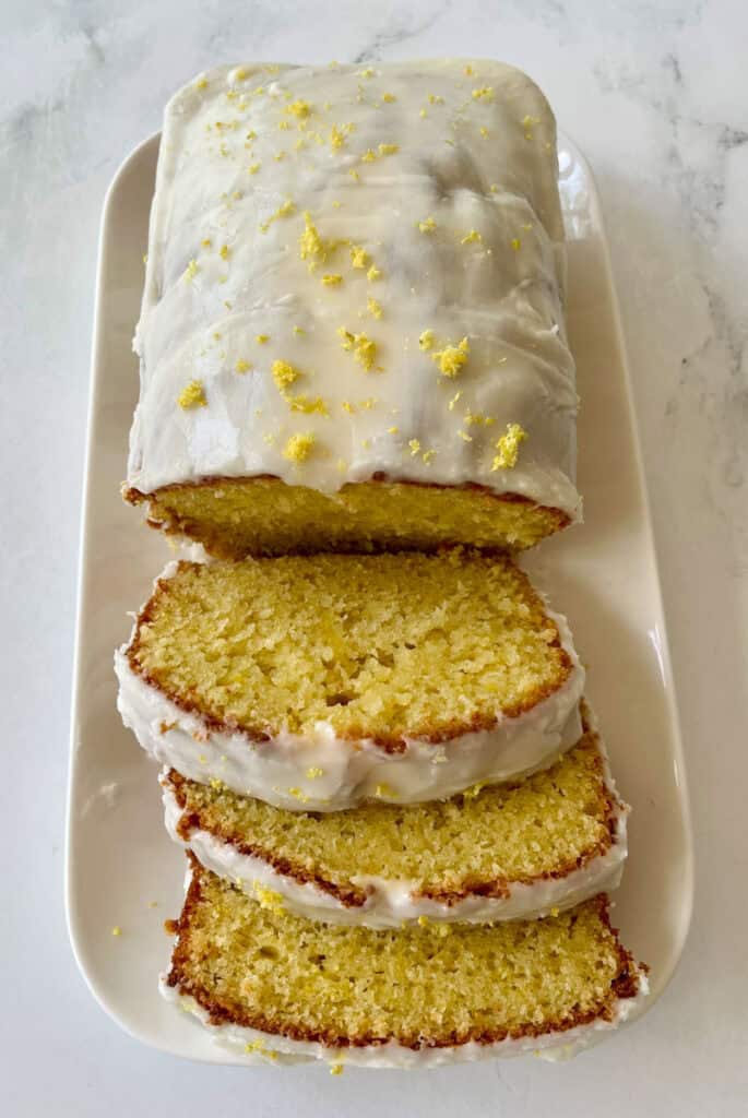 Freshly baked lemon loaf sliced on a white platter, showcasing its moist texture and zesty lemon topping.