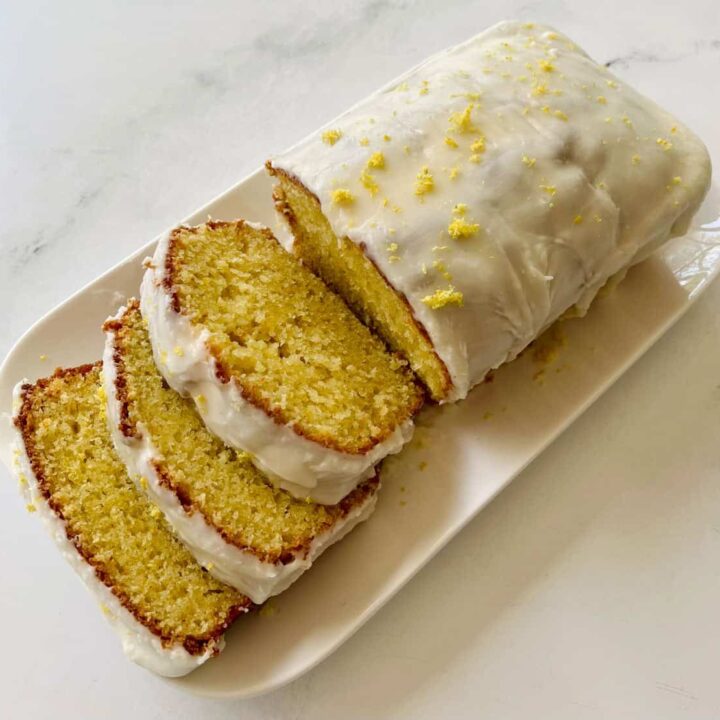 Freshly baked lemon loaf sliced on a white platter, showcasing its moist texture and zesty lemon topping.