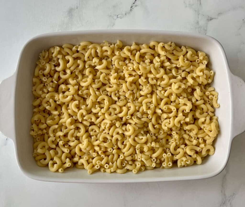 Cooked macaroni pasta in a white casserole dish on a marbled counter.