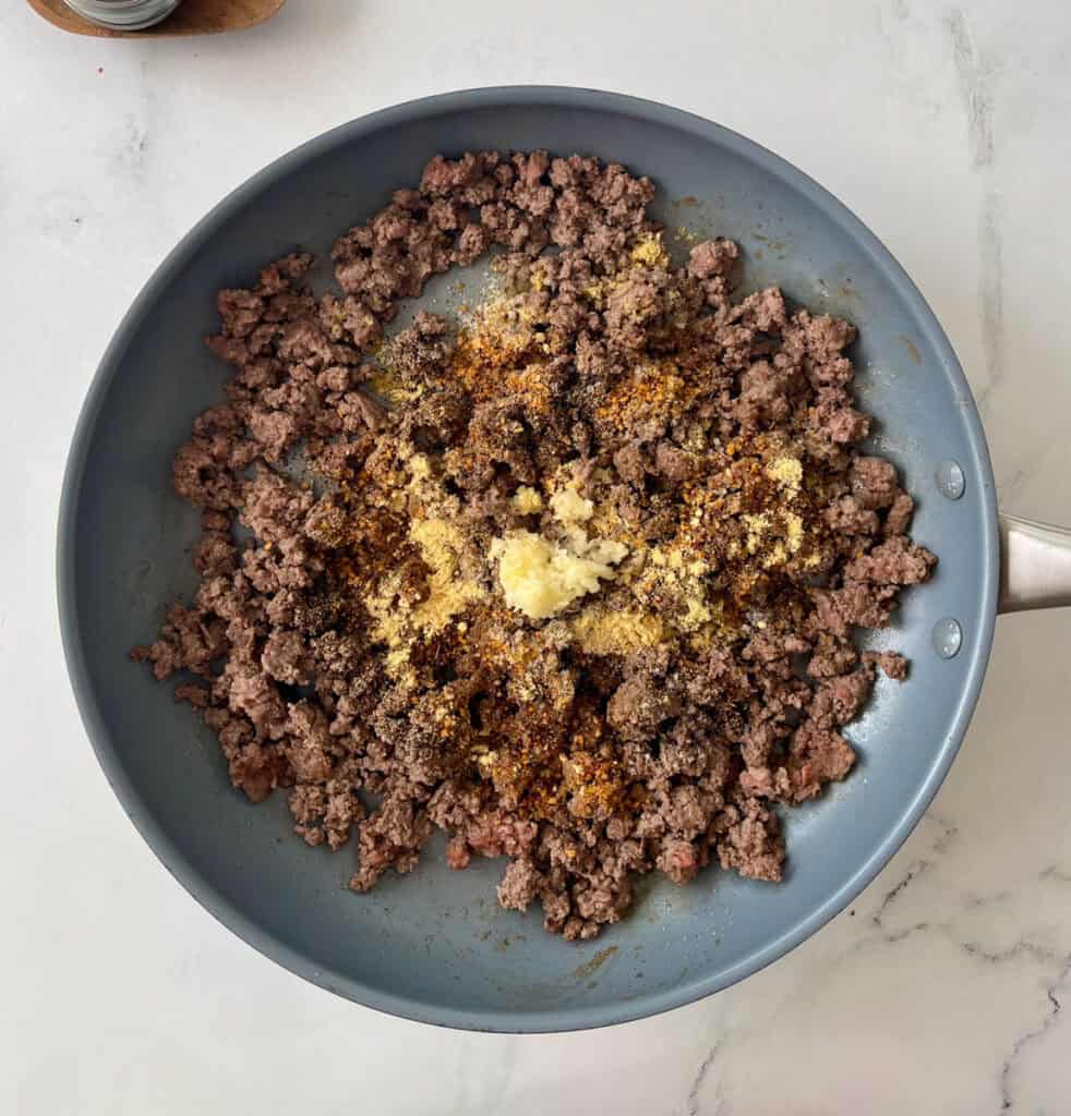 Ground beef cooking with garlic and spices in a skillet.
