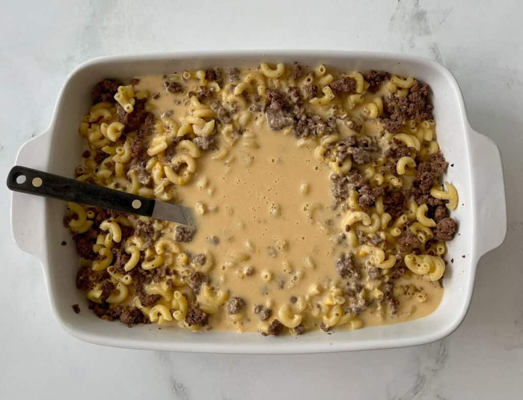 Macaroni with seasoned ground beef and creamy cheese sauce in a casserole dish before baking.