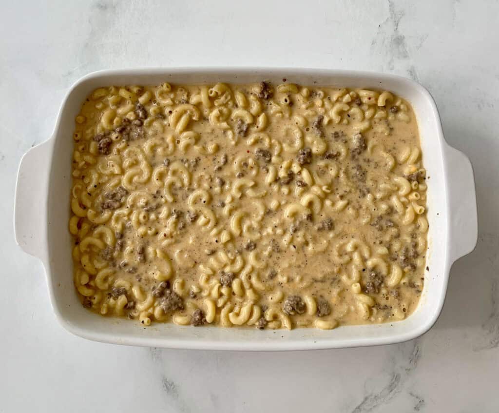 Creamy beef macaroni casserole in a white baking dish, ready to bake.