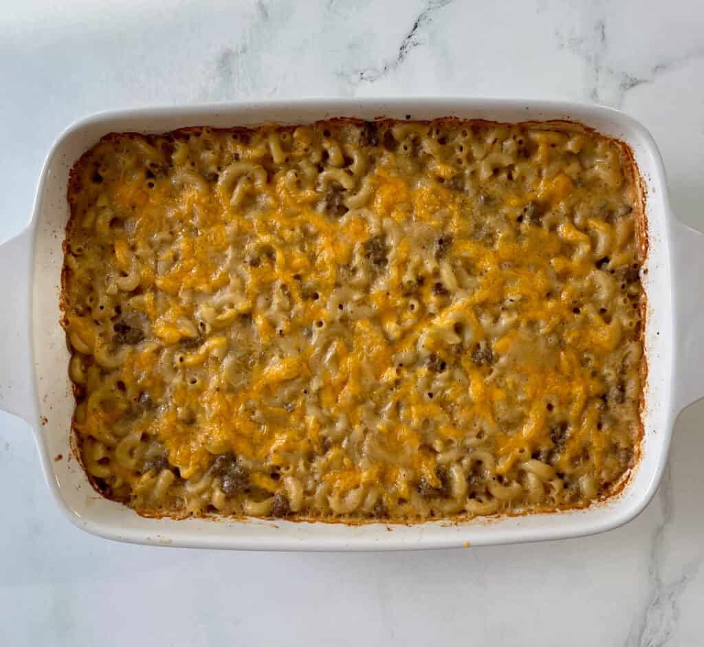 Baked cheesy beef pasta casserole topped with melted cheese, served in a white baking dish.