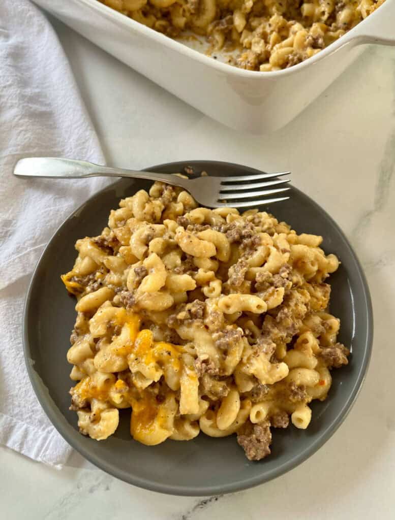 A hearty, cheesy macaroni and cheese with ground beef and melted cheese, served on a dark plate with a fork.