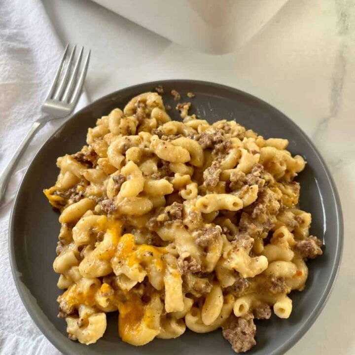 A hearty, cheesy macaroni and cheese with ground beef and melted cheese, served on a dark plate with a fork.