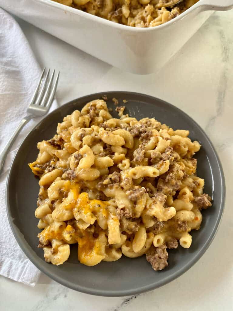 A hearty, cheesy macaroni and cheese with ground beef and melted cheese, served on a dark plate with a fork.