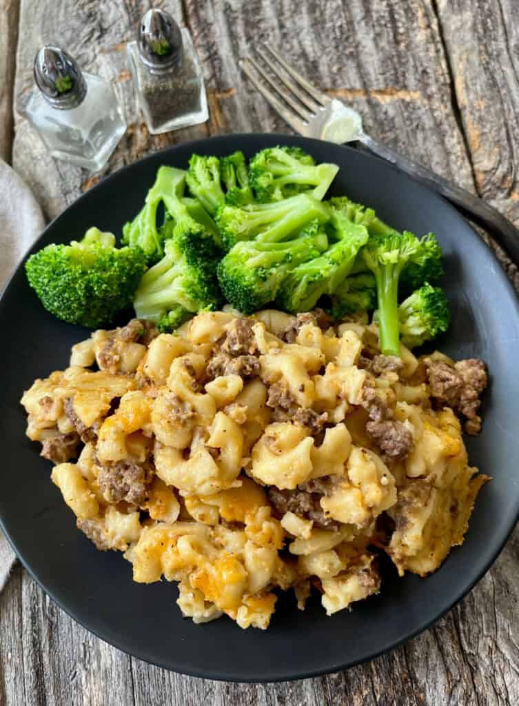 Delicious cheesy beef and mac casserole served on a black plate with fresh broccoli on the side.