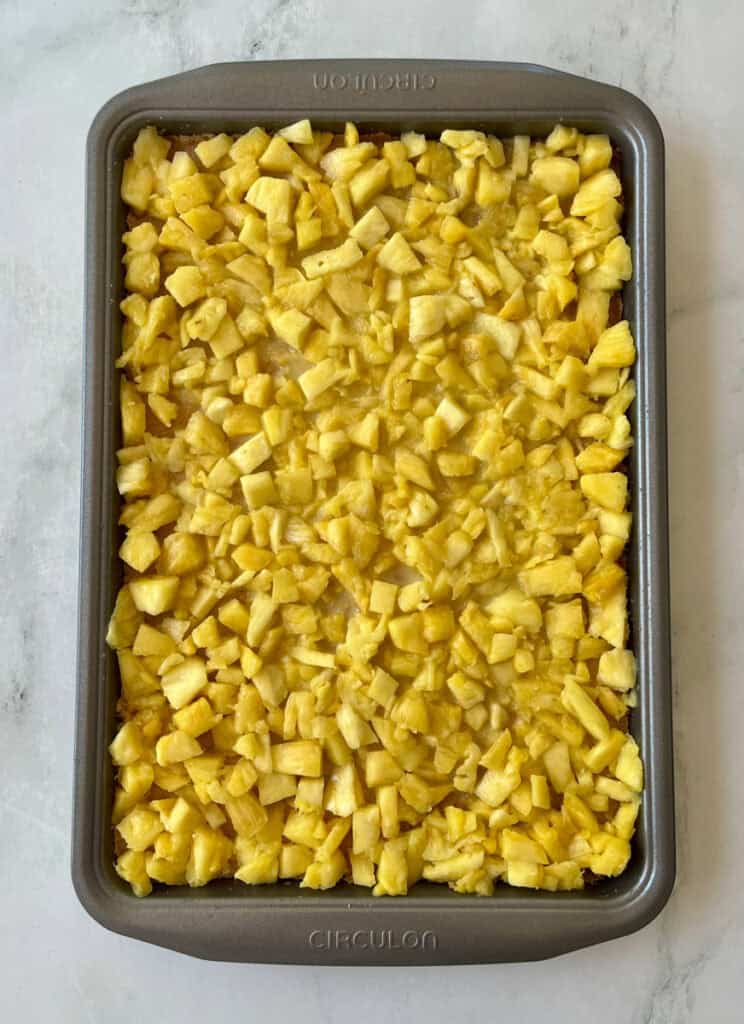 Pineapple mixture with chunks of fresh pineapple spread over a crust in a rectangle pan ready for baking.