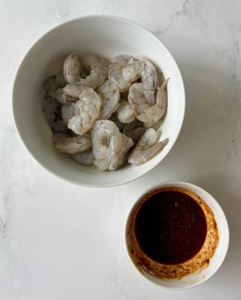 Large bowl of raw shrimp with a bowl of chipotle sauce on a marbled surface.