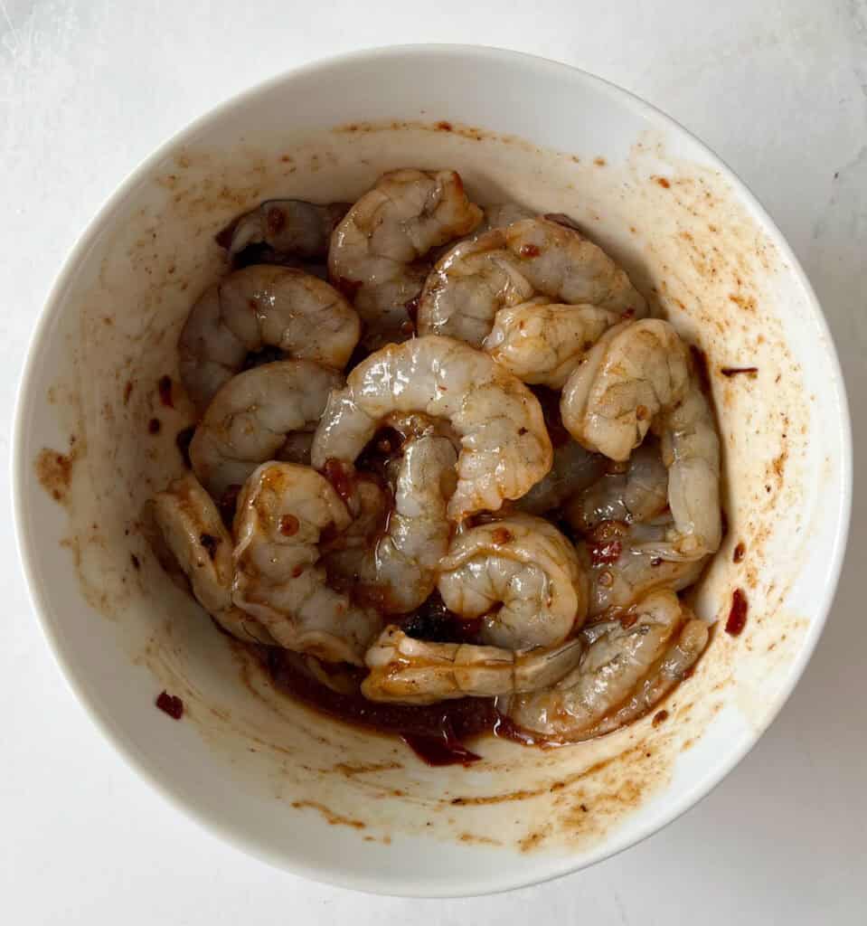 Fresh raw shrimp tossed in a chipotle sauce in a white bowl.