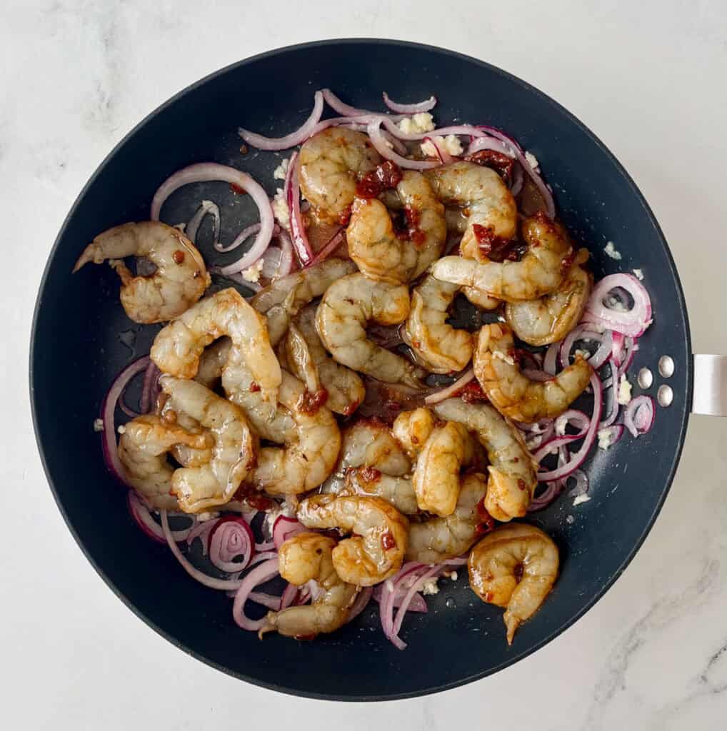Fresh shrimp sauté with red onions in a black skillet.