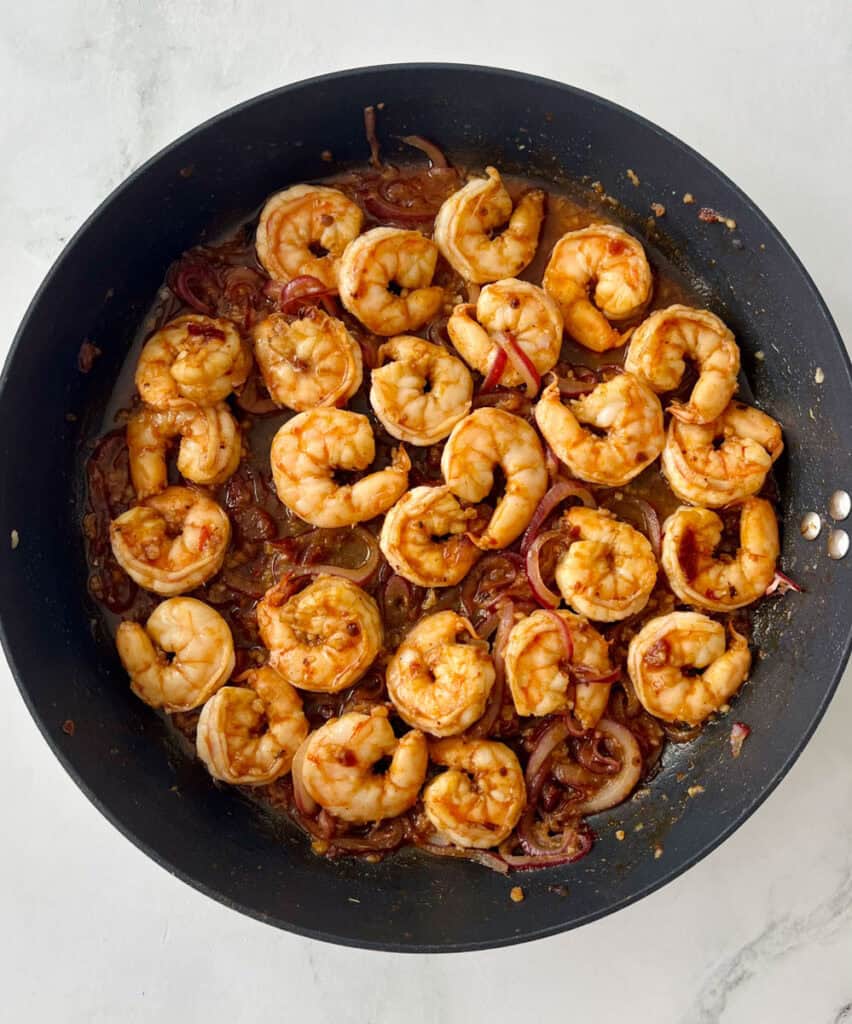 Cooked shrimp with caramelized onions in a black skillet, ready to serve.