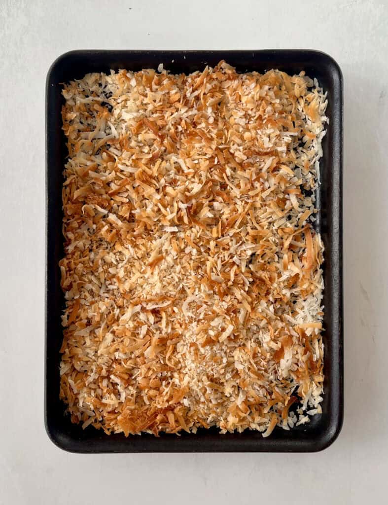 Toasted coconut flakes on a dark baking pan.