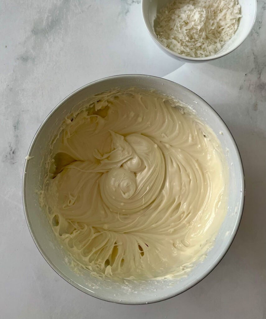 Delicious homemade coconut cream frosting there is a bowl of coconut flakes.