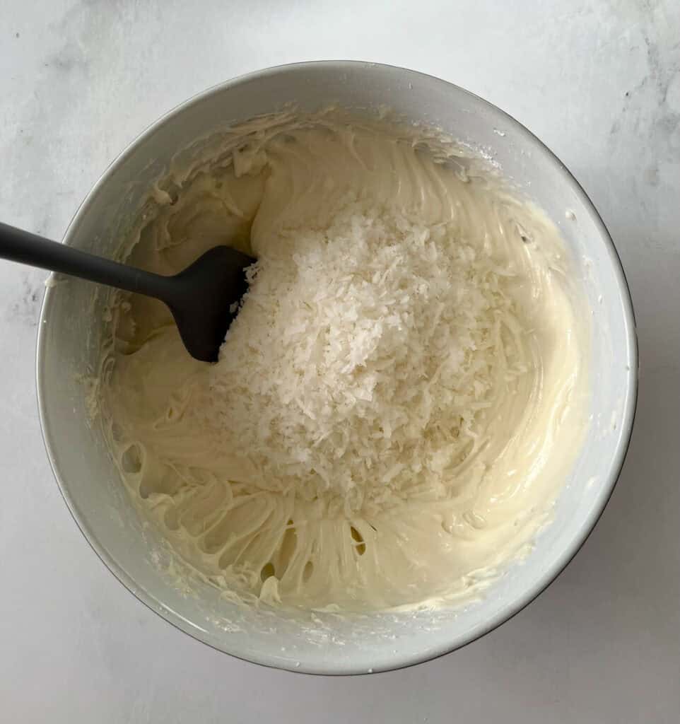 Delicious coconut frosting in a mixing bowl with shredded coconut on top.