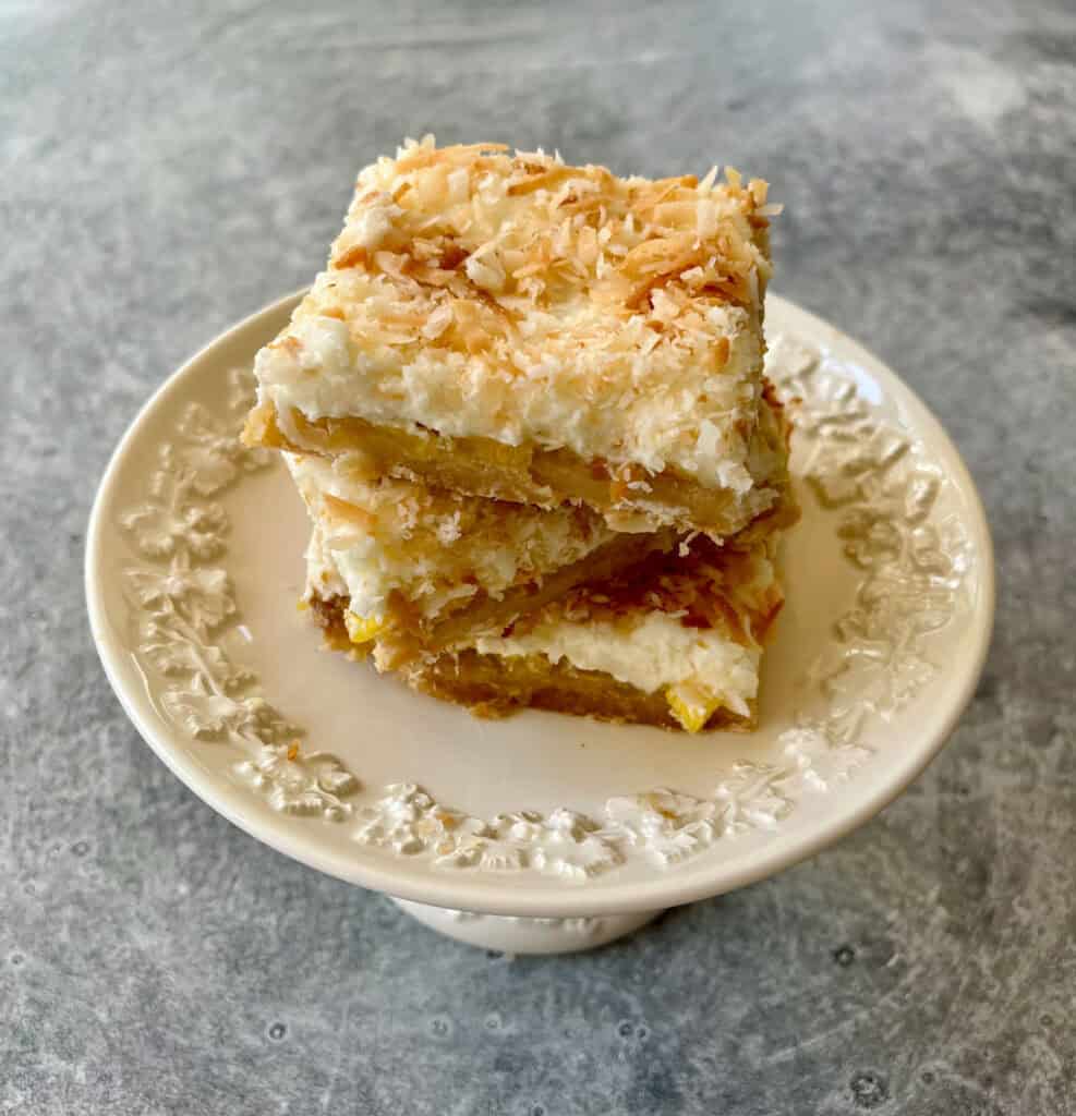 Close-up image of pineapple bars with toasted coconut topping on a white plate.