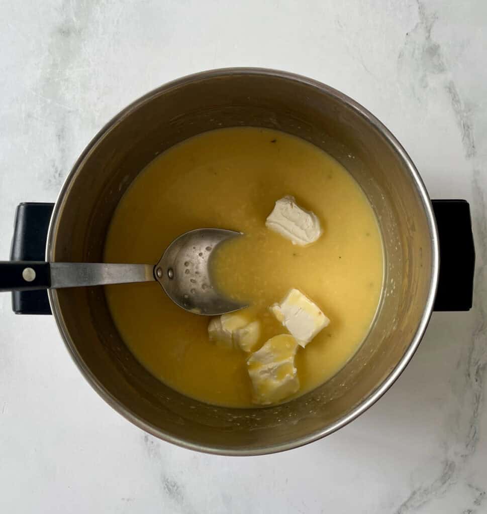 Chicken broth, condensed soup, and cream cheese melting in a saucepan on a marbled surface.