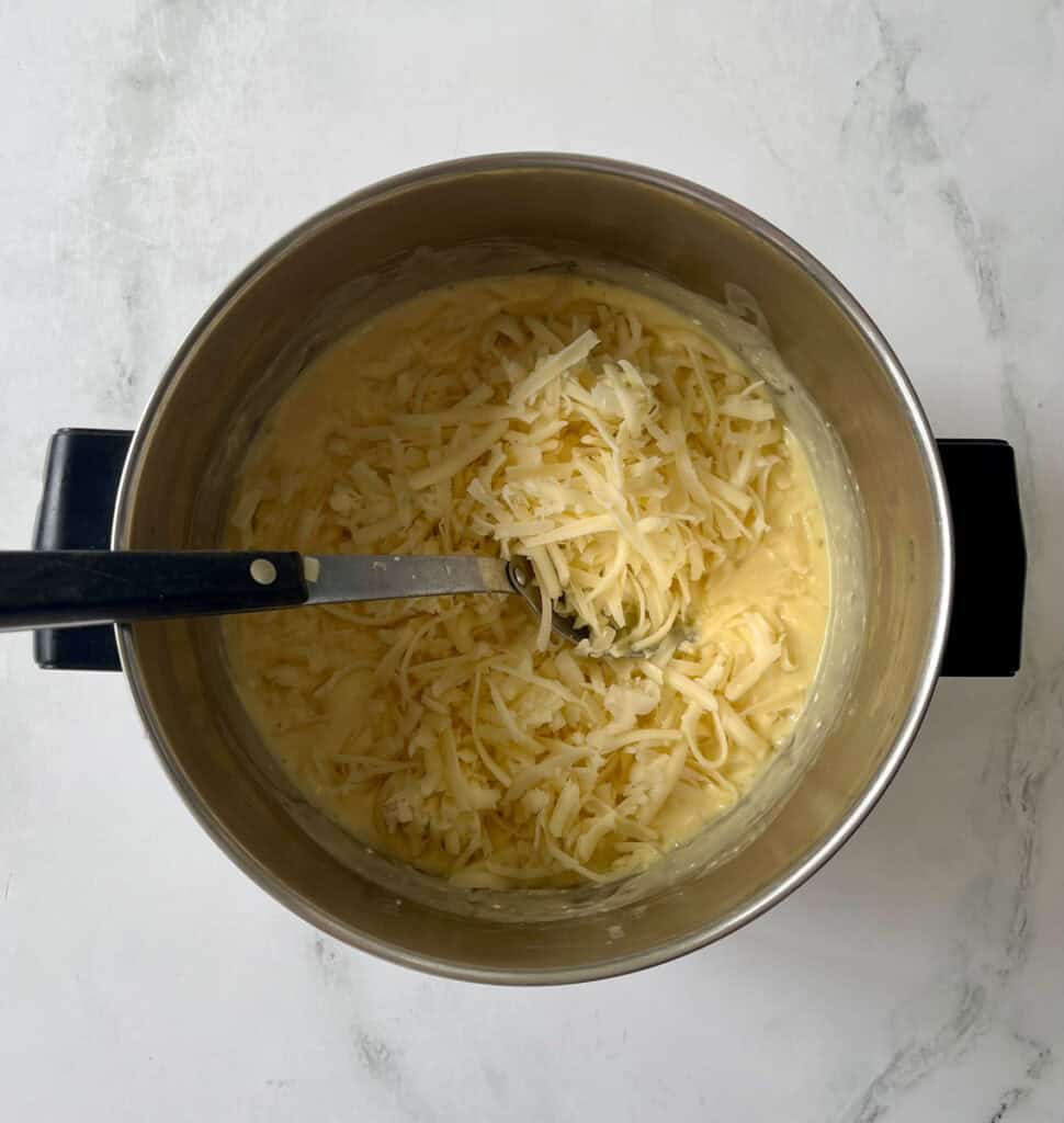 Cheese melting in a pot of sauce on a marbled surface.