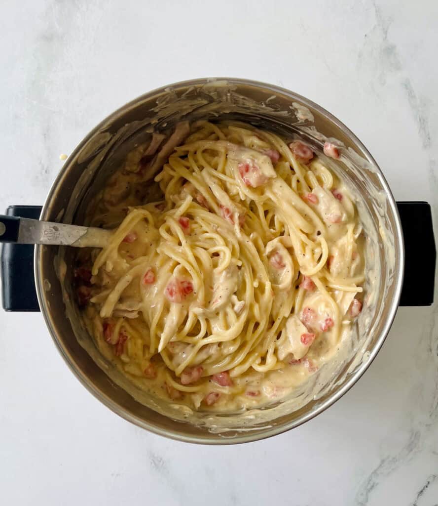 Creamy chicken spaghetti in a pot, on a marbled surface.