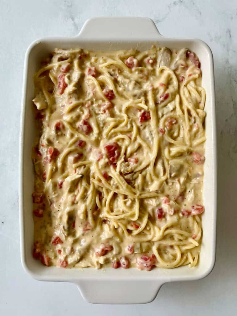Unbaked creamy chicken spaghetti in a white baking dish on marble surface.