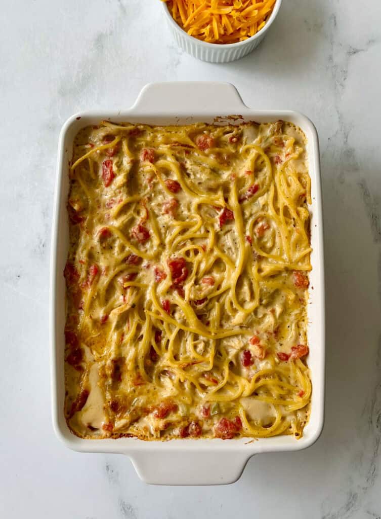 Baked creamy chicken spaghetti with tomatoes in a white dish on a marbled surface.