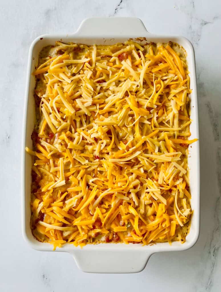 Cheesy chicken spaghetti casserole topped with shredded cheese in a white dish.