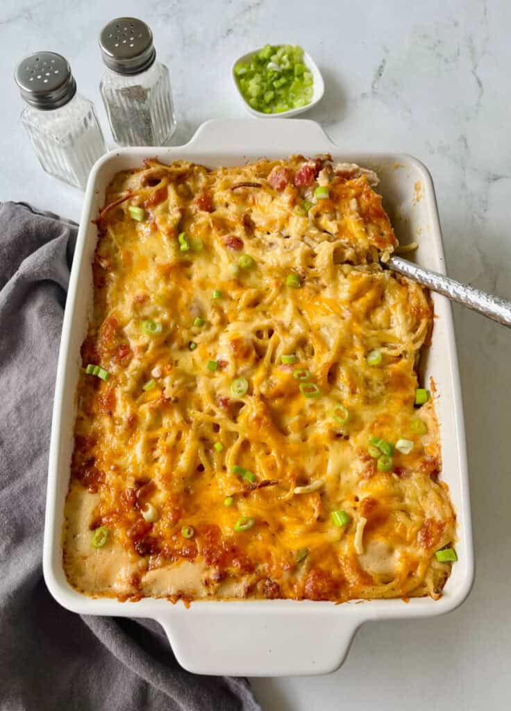 Baked cheesy chicken spaghetti casserole with green onions in a white dish.