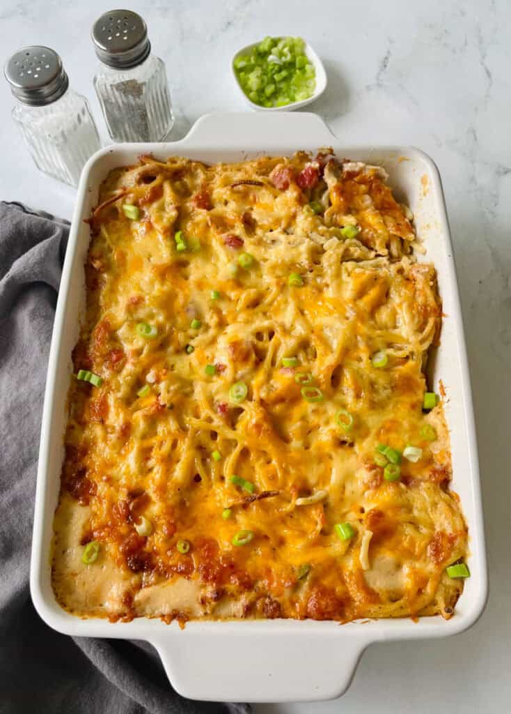 Baked cheesy chicken spaghetti casserole with green onions in a white dish.