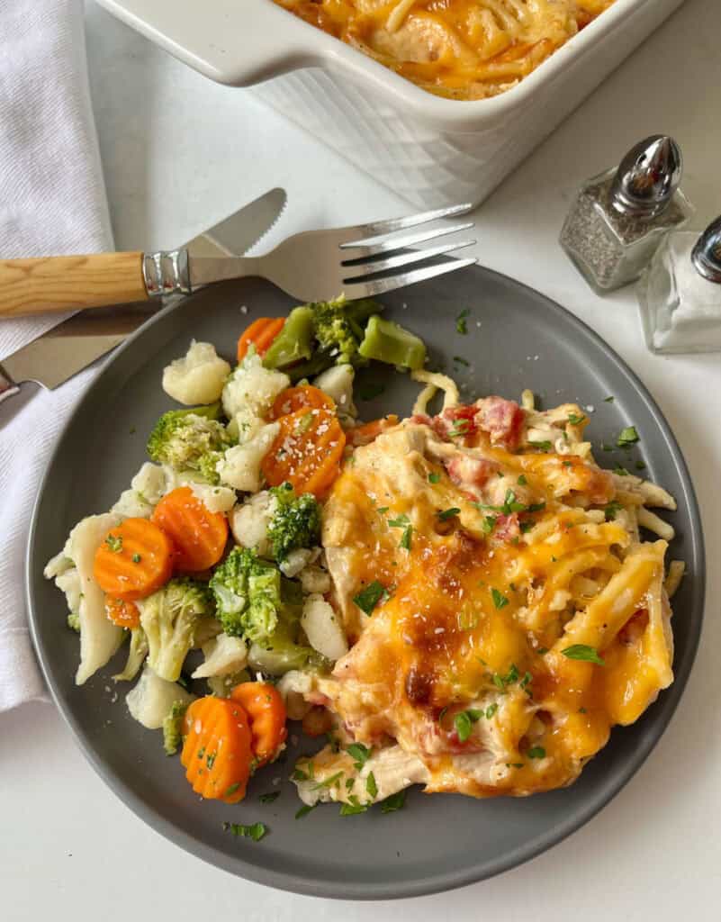 Baked cheesy chicken spaghetti with mixed vegetables on a gray plate.