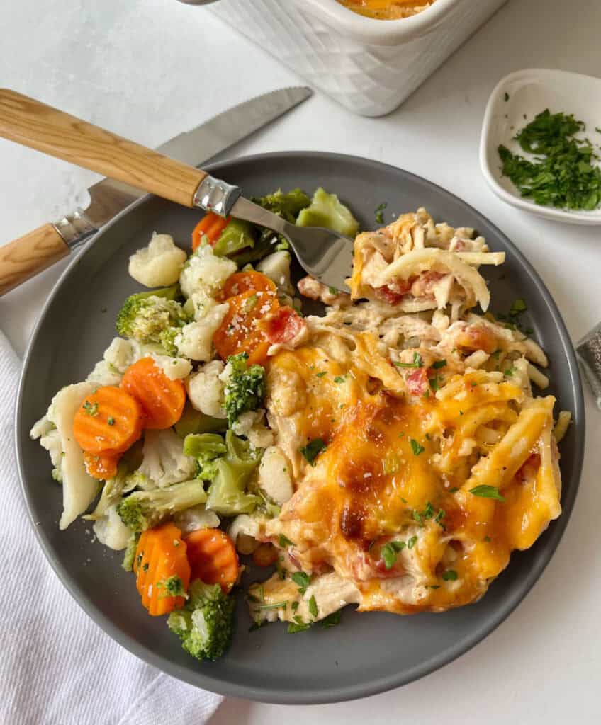 Baked chicken spaghetti casserole with cheese, served with steamed vegetables on a gray plate.