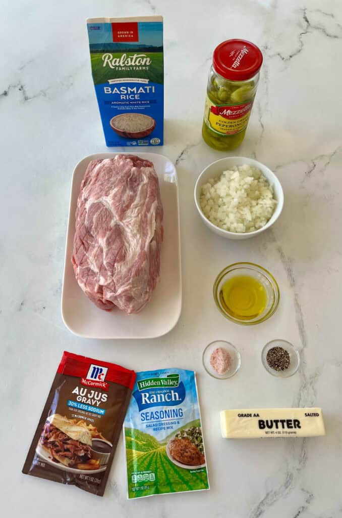 Raw pork roast, rice, seasonings, and cooking ingredients on marble surface.