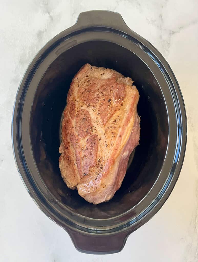 Raw seasoned pork roast in slow cooker for cooking.