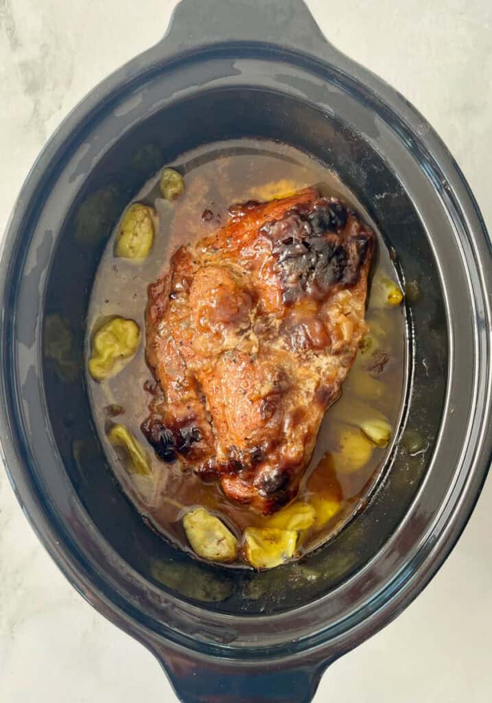 Slow cooker pork roast with pepperoncini peppers in a black crockpot.