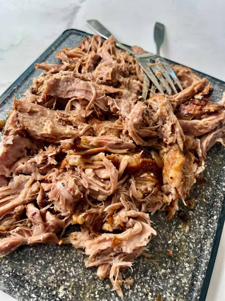 Tender shredded pulled pork on a grey cutting board with forks.