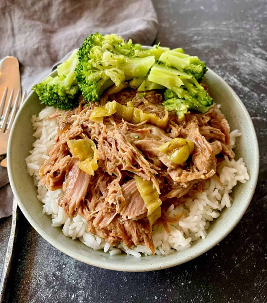 Pulled pork served over rice with steamed broccoli on a white bowl.