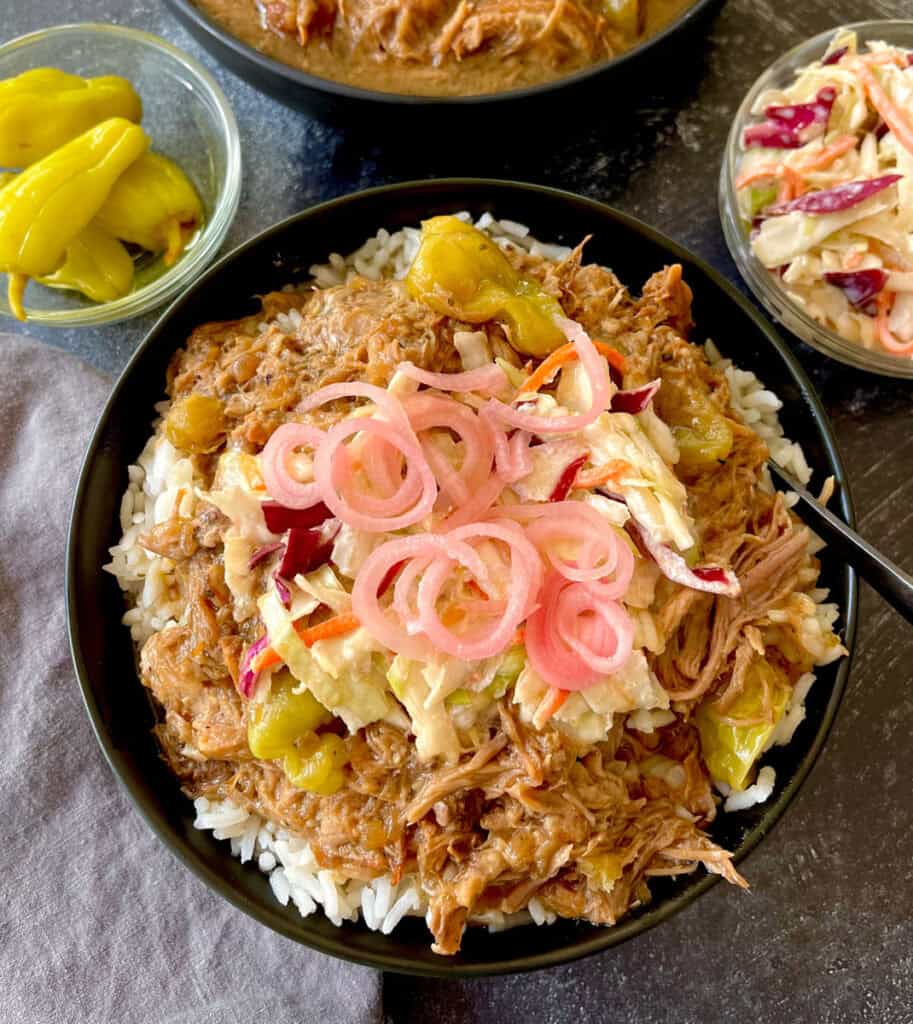 Pulled pork rice bowl topped with pickled onions and coleslaw. With side dishes of peppers and coleslaw.