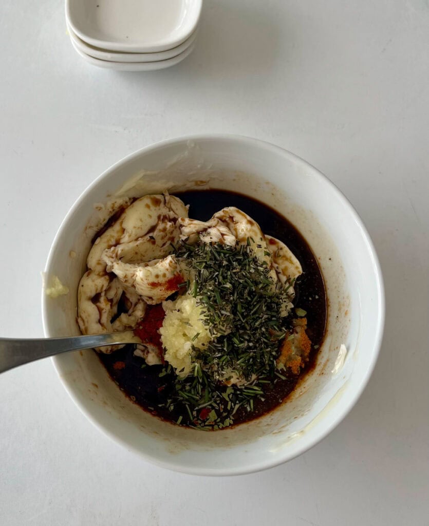 Butter mixture with herbs, garlic, and sauce in a white bowl.
