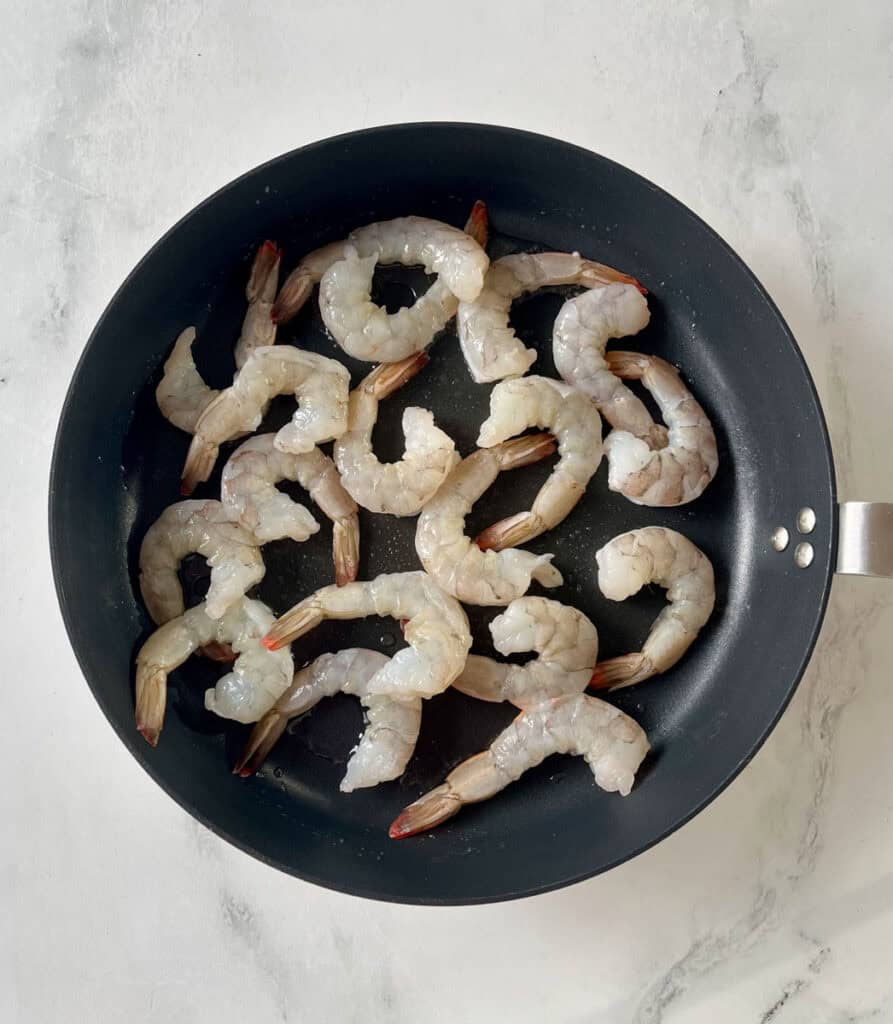 Fresh raw shrimp in a black frying pan cooking.