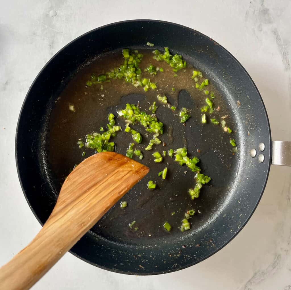 Cooking chopped green onions in a black non-stick skillet with a wooden spatula.