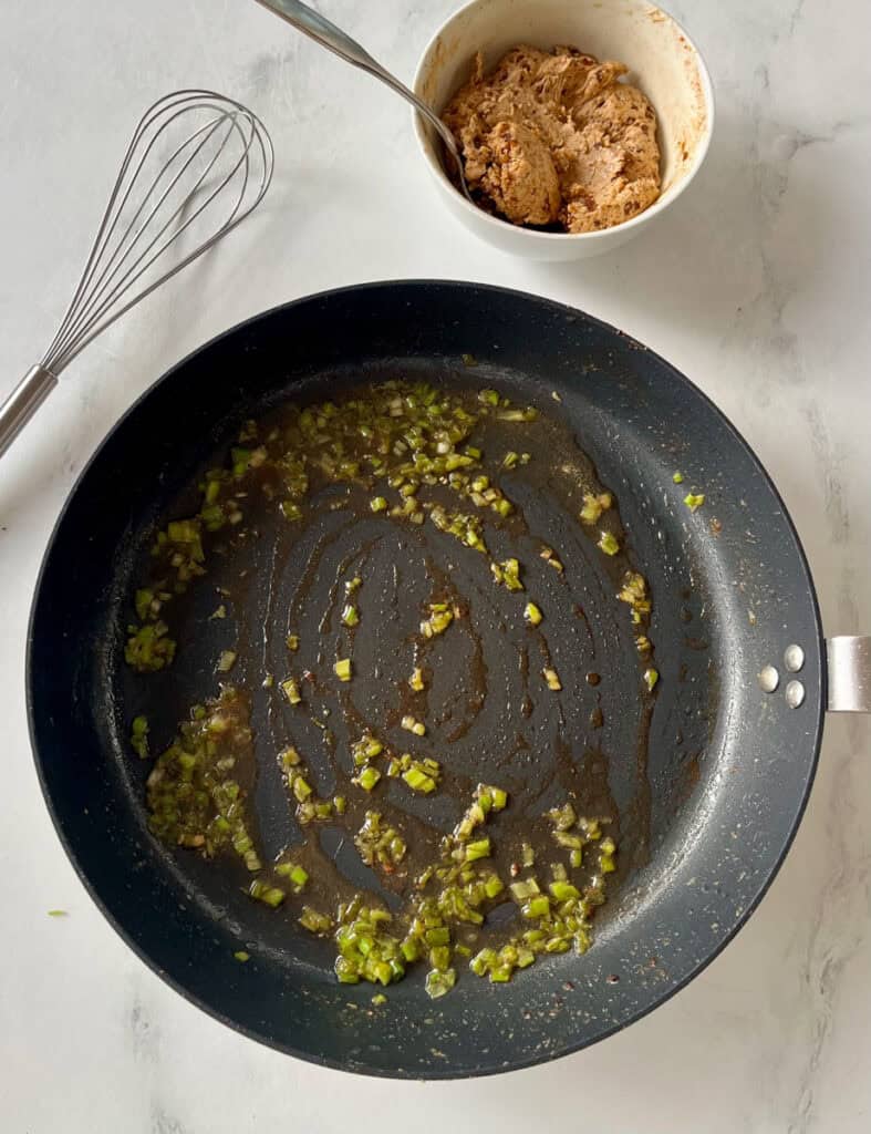 Sautéed green onions and white white in a black skillet for recipe preparation.
