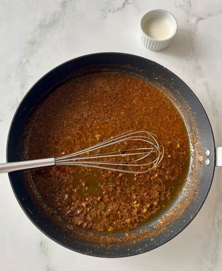 Herbed butter and wine cooking in a skillet with a whisk and a small bowl of cream.