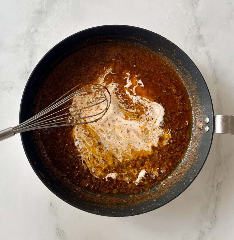 Sauce being prepared in a black pan with a whisk inside.