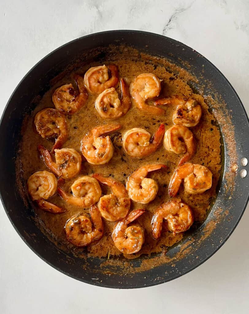 Shrimp cooked in garlic butter sauce in a black skillet on a white surface.