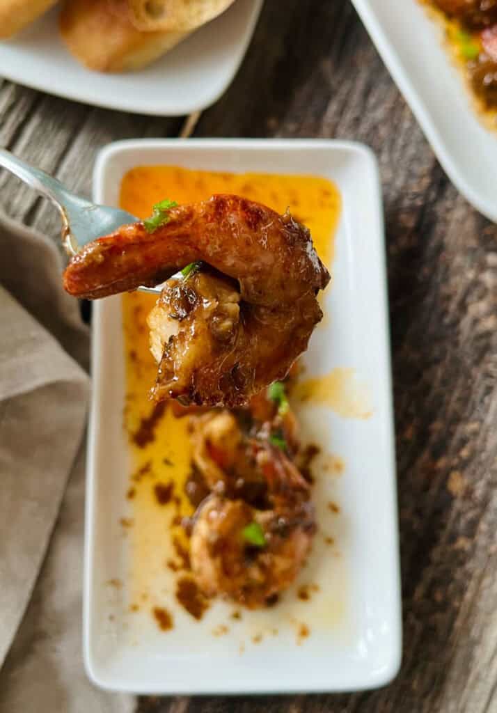 Close-up of a sautéed shrimp dipped in sauce on a white dish.