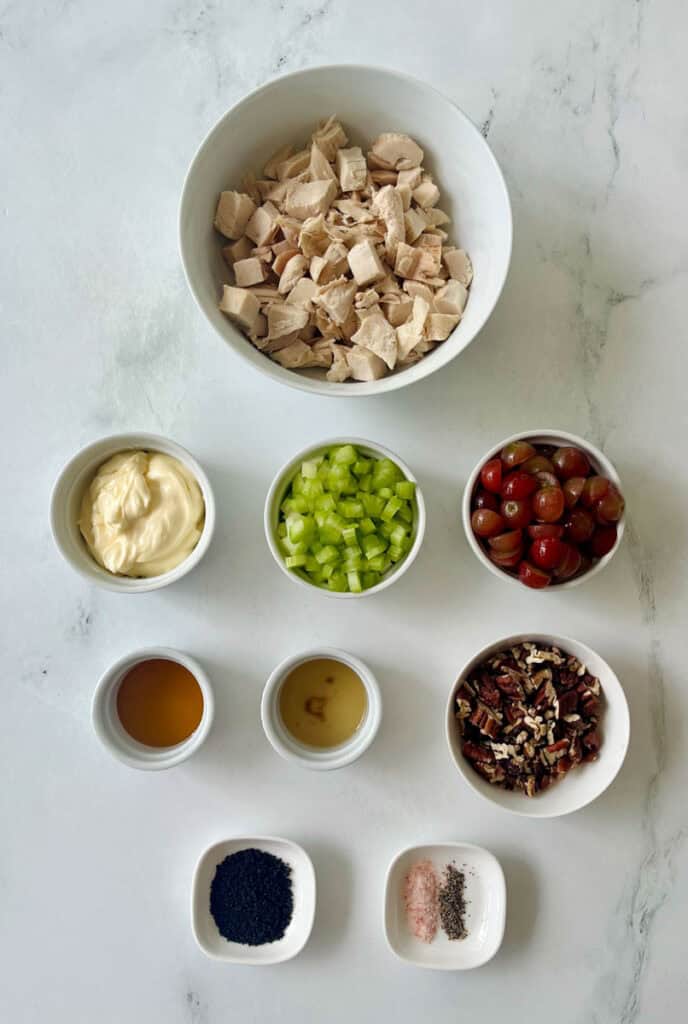 Ingredients for homemade chicken salad including cooked chicken, celery, pecans, grapes, mayonnaise, and seasonings.