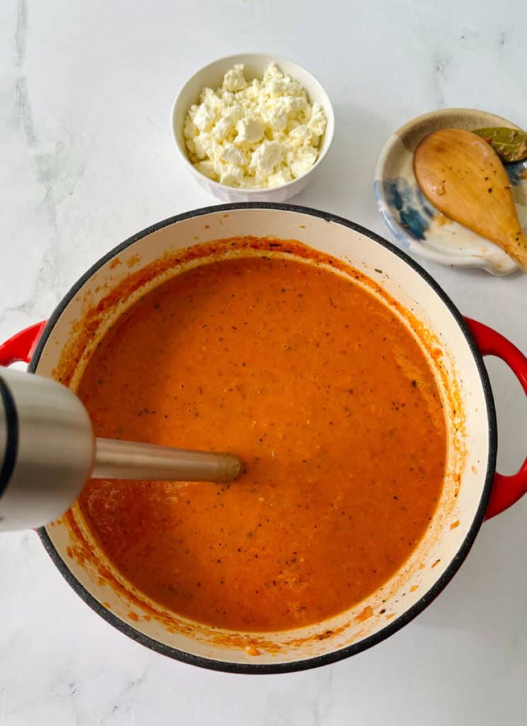 A pot of creamy tomato soup with basil and spices, ready to serve.